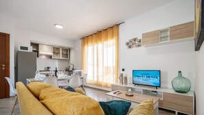 A modern living room with a sofa, a TV, and a dining area with chairs and a table. - Holiday Apartment "Cambrils Turistic Atico" with Private Terrace & Wi-Fi (Cambrils)