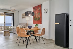 A modern living room with a dining area, a black refrigerator, and a large window with a view.