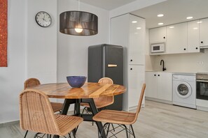 Una cocina moderna con comedor, que incluye una mesa redonda de madera, sillas de mimbre, un refrigerador negro, un microondas y una lavadora.