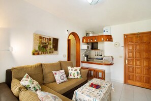 A living room with a sofa, a small table, a kitchen area, and a wooden door.