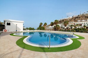 A swimming pool with a unique design, surrounded by a tiled deck and green artificial grass.