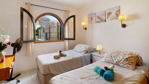 A hotel room with two beds, a window with curtains, a desk with a chair, and a wall-mounted lamp. - Vacation Apartment 'Residencial Sol Suite 2' with Sea View, Shared Pool and Wi-Fi (Puerto Rico)
