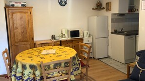 Cocina compacta con microondas, cafetera y refrigerador. Hay una mesa de comedor con sillas y un armario.