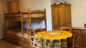 Una cama individual con dos literas, un cabecero de madera, un mueble pequeño y una mesa redonda con mantel floral.