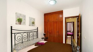 A bedroom with a bed, a wooden wardrobe, a small table with a lamp, and a mirror. - Vacation Home 'Residencial Sol Suite' with Private Terrace, Balcony and Wi-Fi (Telde, Gran Canaria)