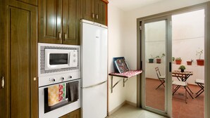 A kitchen with wooden cabinets, a white refrigerator, a microwave, and an oven. There is a small table with chairs and a potted plant outside. - Vacation Home 'Residencial Sol Suite' with Private Terrace, Balcony and Wi-Fi (Telde, Gran Canaria)