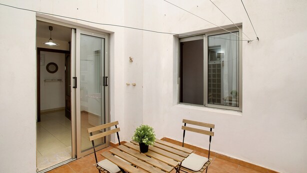 A patio with a wooden table and chairs, a potted plant, and a sliding glass door leading to an interior space. - Vacation Home 'Residencial Sol Suite' with Private Terrace, Balcony and Wi-Fi (Telde, Gran Canaria)