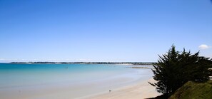 A beach with clear water, a sandy shore, and a distant shoreline with buildings.