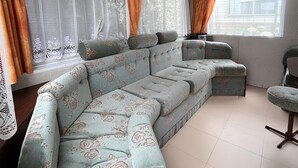 Un sofá modular con estampado floral, una mesita redonda y un ventanal con cortinas.