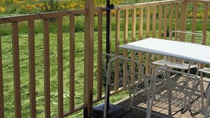 A wooden deck with a table and chairs under a canopy, overlooking a grassy landscape.
