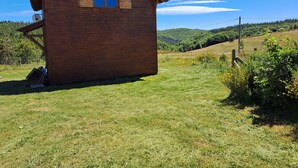 A wooden cabin with a sloped roof, a small porch, and a clear view of a hilly landscape.