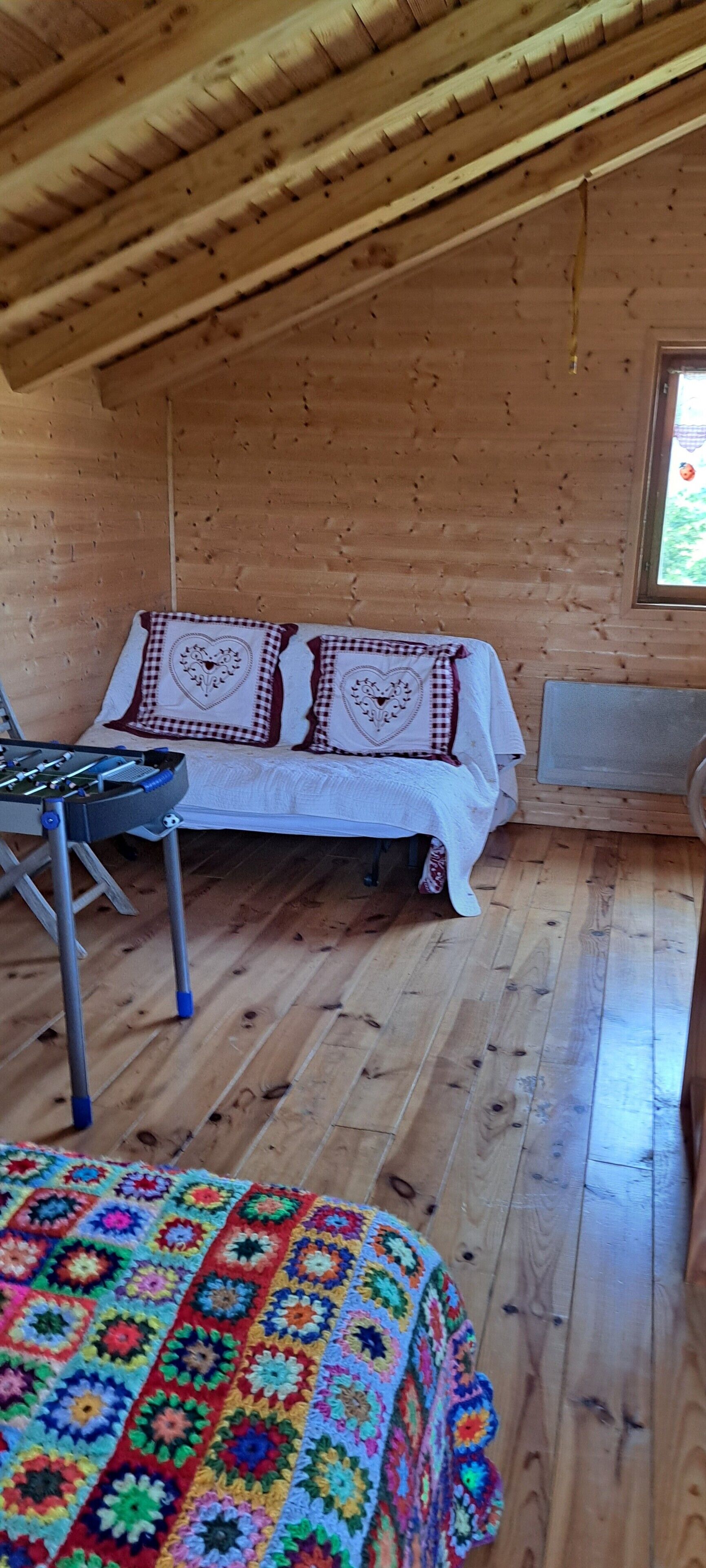 A cozy wooden room with a bed, a table, and a colorful blanket.