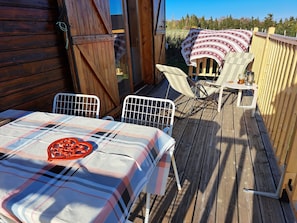 A wooden deck with a table and chairs, a covered area with a blanket, and a wooden fence.