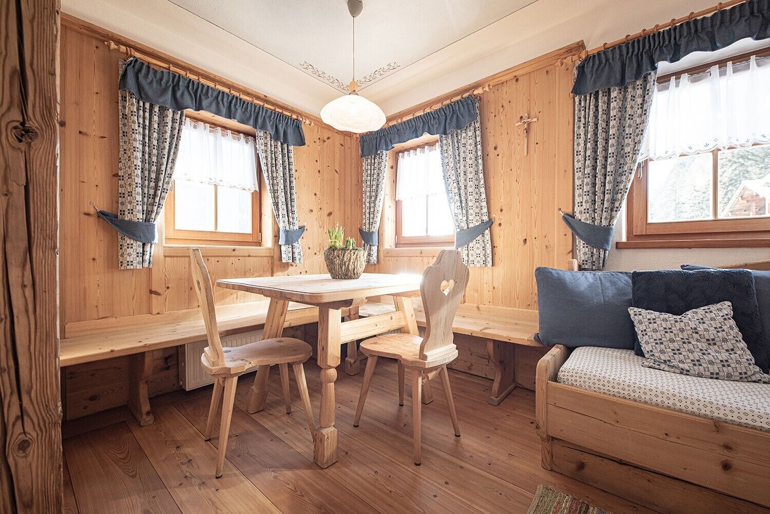 A wooden interior with a dining table, chairs, a sofa, and curtains.