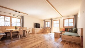 Une pièce spacieuse dotée d’un plancher en bois, d’un coin repas avec des chaises et une table, d’un canapé avec des coussins, d’une télévision et de grandes fenêtres.