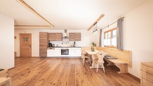 Une cuisine moderne avec des meubles en bois, un coin repas avec un banc et une fenêtre agrémentée de rideaux.
