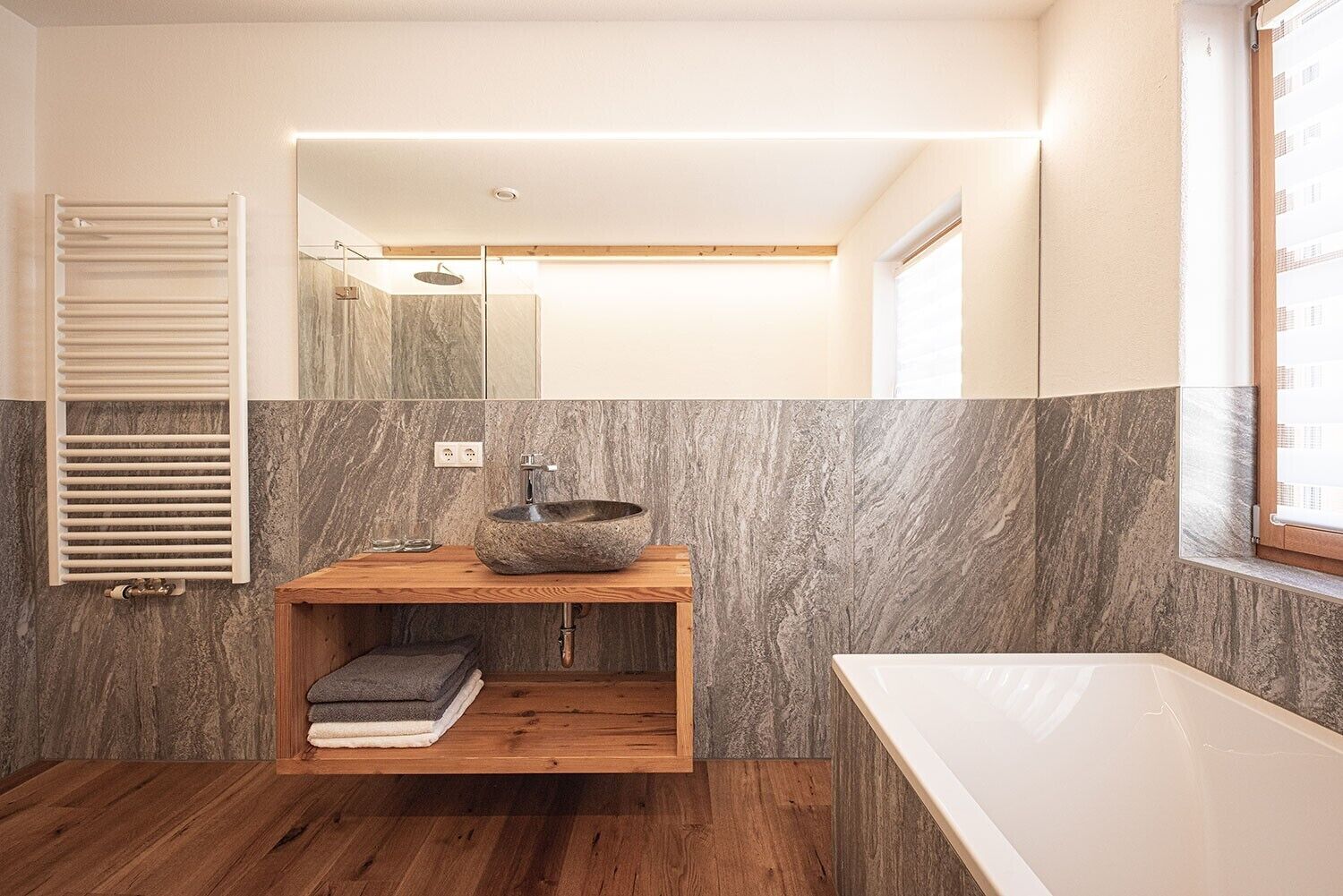 Un baño moderno con un tocador de madera, un lavabo de piedra y una bañera blanca.
