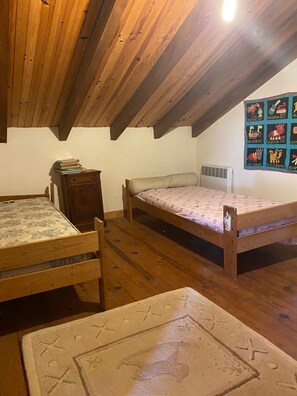 Una habitació petita i acollidora amb sostre de fusta, una llitera, escriptori i una còmoda.