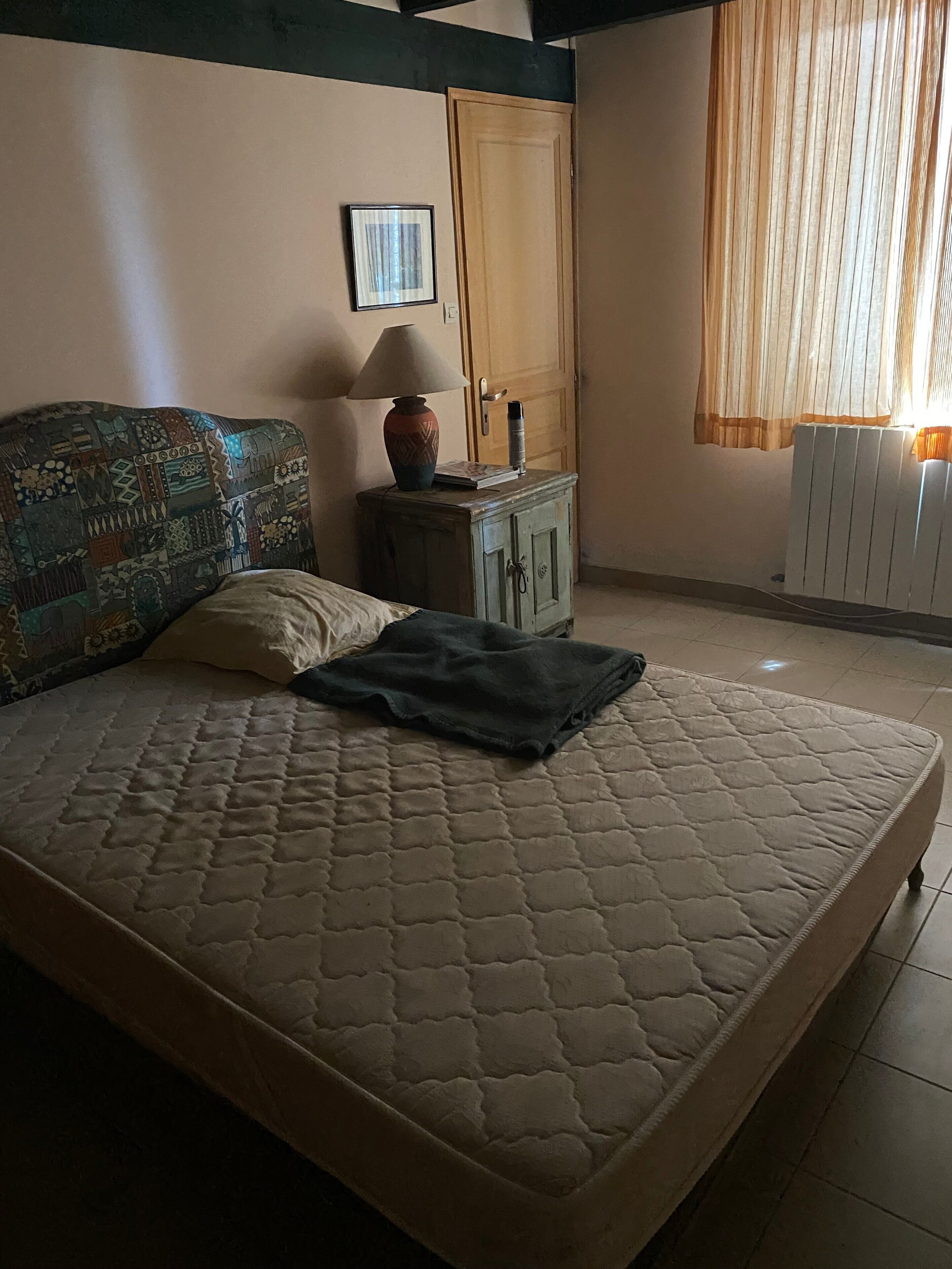 A bedroom with a bed, a nightstand, a lamp, a door, and a window with curtains.