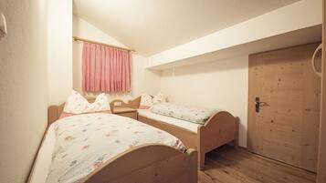 Un petit logement composé d’une seule pièce, avec deux lits en bois, une porte en bois et une fenêtre ornée d’un rideau à carreaux.