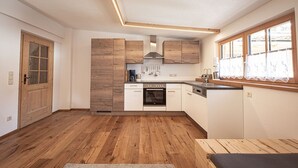 Een kleine keuken met houten kastjes, een ingebouwde oven en een raam met gordijnen.
