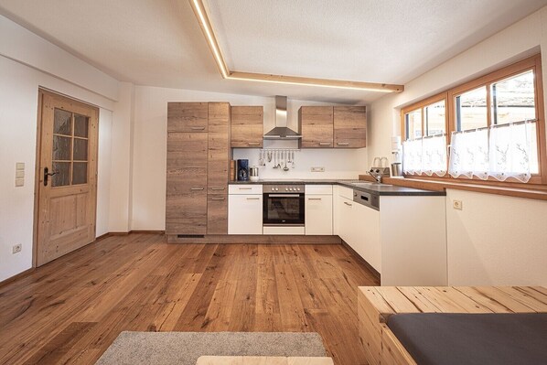 Cocina compacta con armarios de madera, horno integrado y ventana con cortinas.