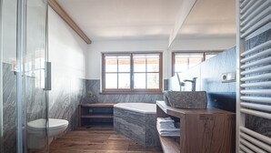 Een badkamer met een glazen douchecabine, een toilet, een badkuip en een wastafel met een stenen wasbak.