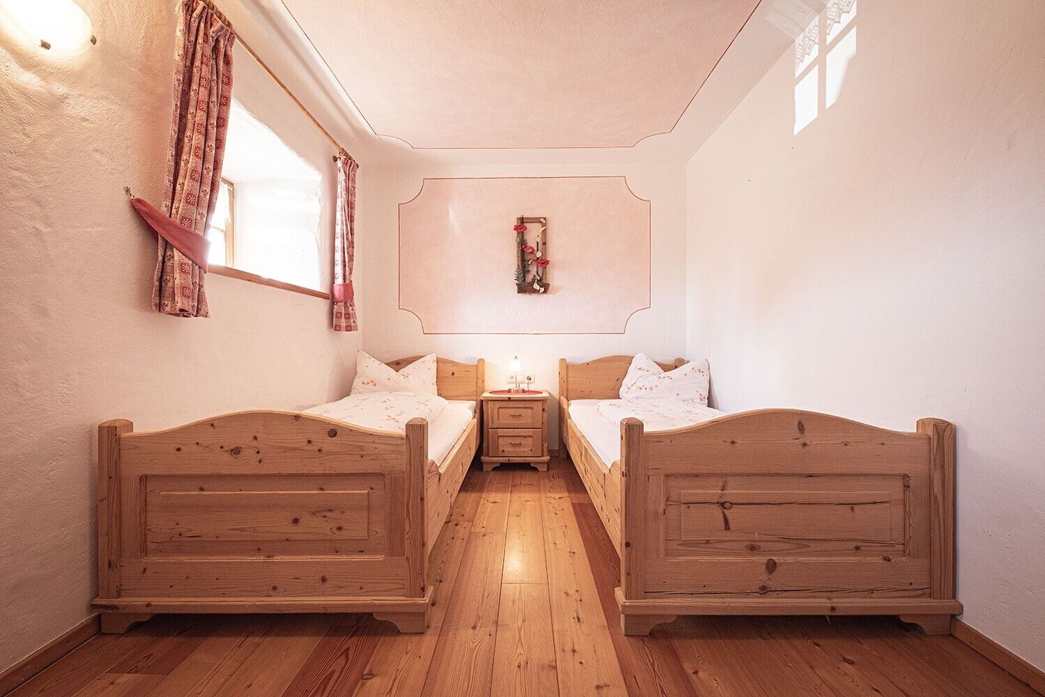Une chambre avec deux lits en bois, une table de chevet, une étagère murale ornée d’un objet décoratif et une fenêtre avec des rideaux.