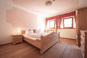 Ein Schlafzimmer mit einem hölzernen Bett, Nachttischen, einer Kommode und einem Fenster mit Vorhängen.