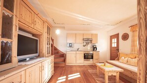 A cozy living room with wooden furniture, a television, a sofa, and a kitchen area with wooden cabinets and appliances. - Holiday Apartment "Himmelschlüssel" with Mountain View, 2 Private Terraces & Wi-Fi (Acereto)