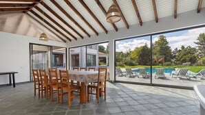 A dining area with a table and chairs, a view of a pool and garden through large glass doors. - Holiday Home 'Quinta Grande' with Private Pool, Private Terrace and Wi-Fi (Chamusca)