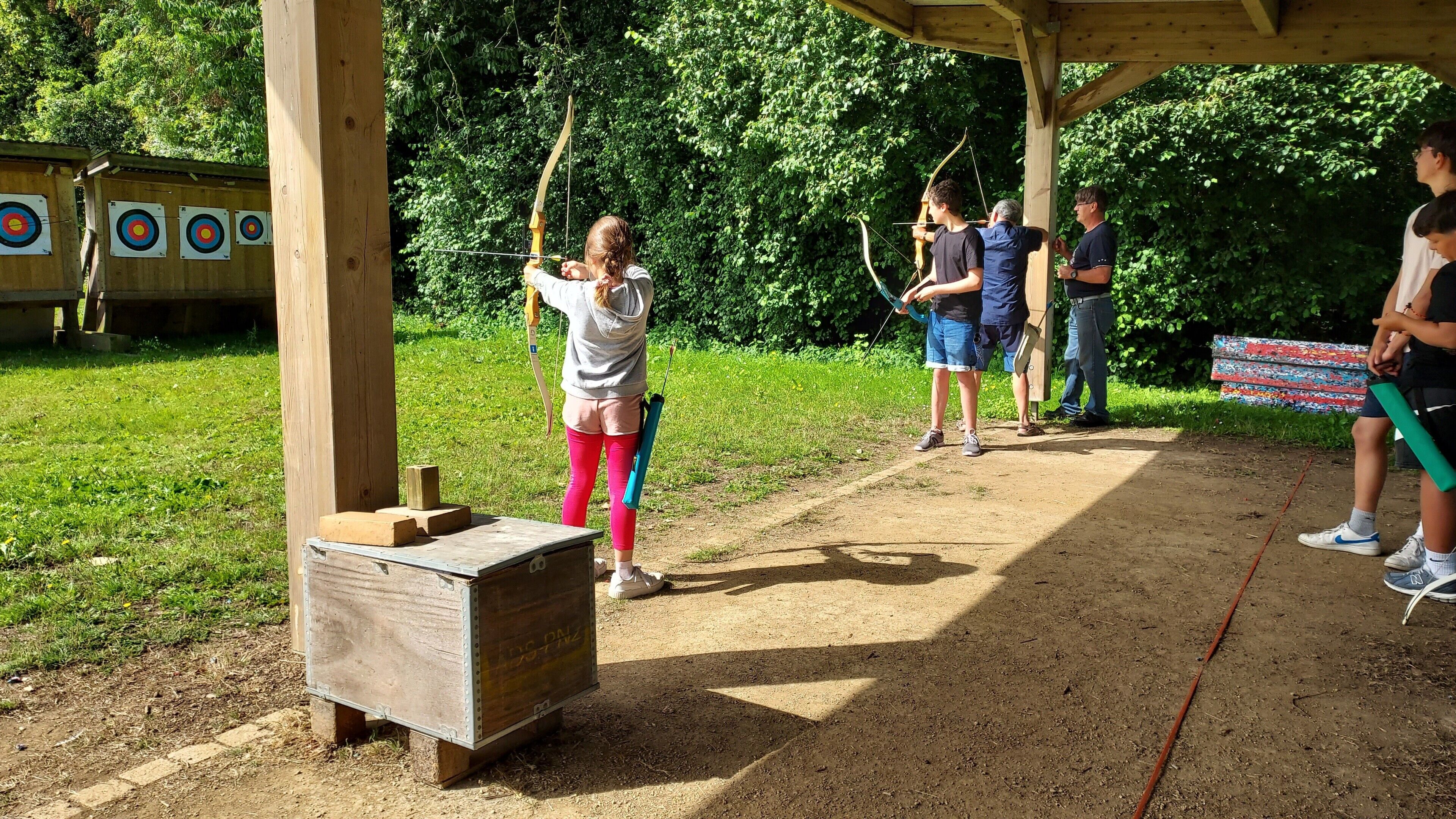 An outdoor archery range with targets, a wooden shooting box, and a covered area.
