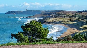 Un paysage côtier avec une plage, des vagues et un phare au loin.