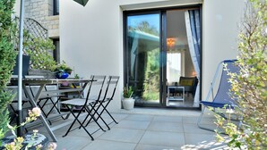 En udendørs terrasse med et bord, stole, en potteplante og en skydedør, der fører ind i et rum.