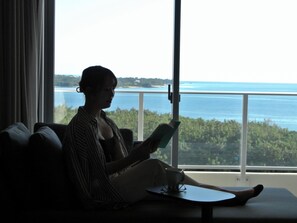 A person sitting on a couch by a window with a view of the sea.