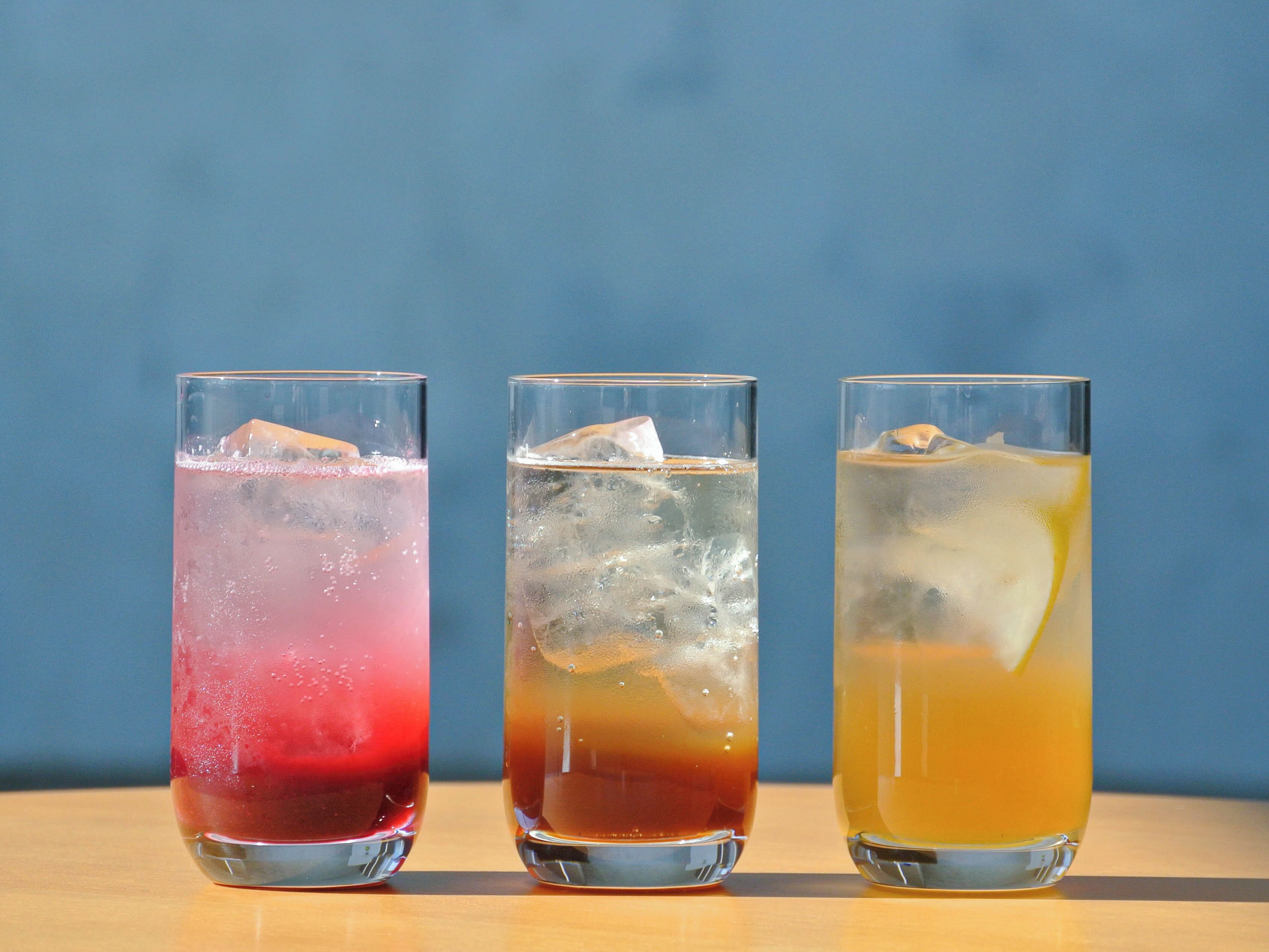 Tres vasos de bebidas de colores distintos sobre una superficie de madera, sobre un fondo azul.