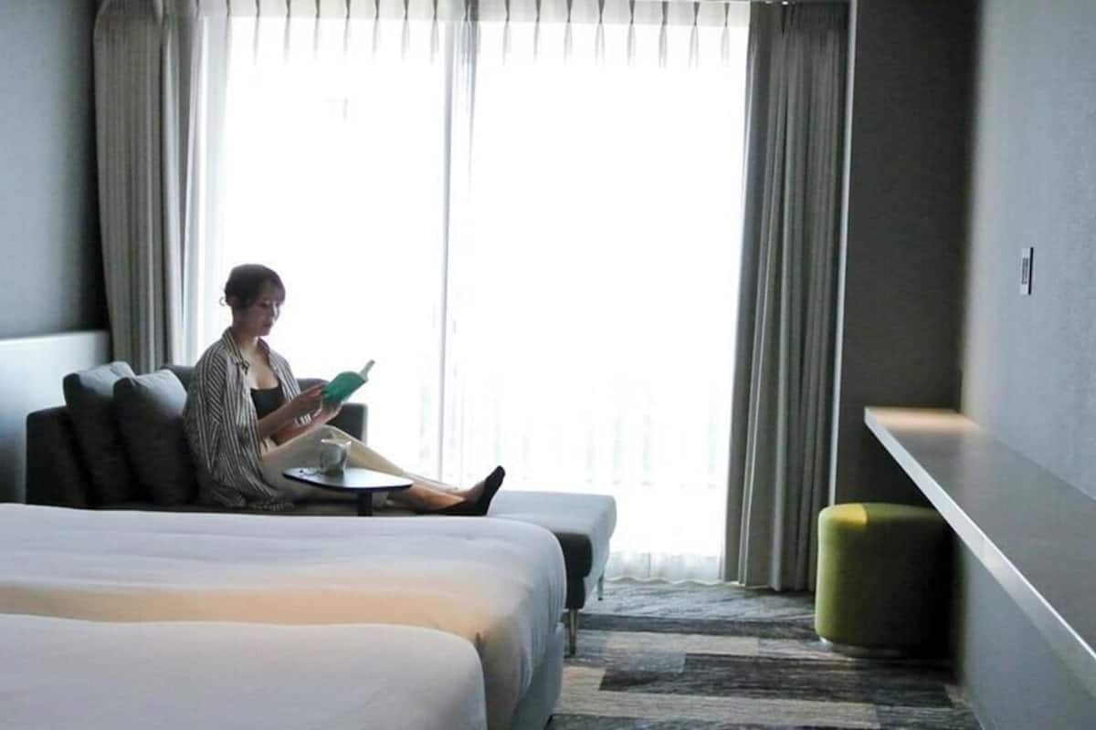 Une chambre d’hôtel comprenant un lit, un coin salon, une fenêtre avec des rideaux et un petit tabouret.