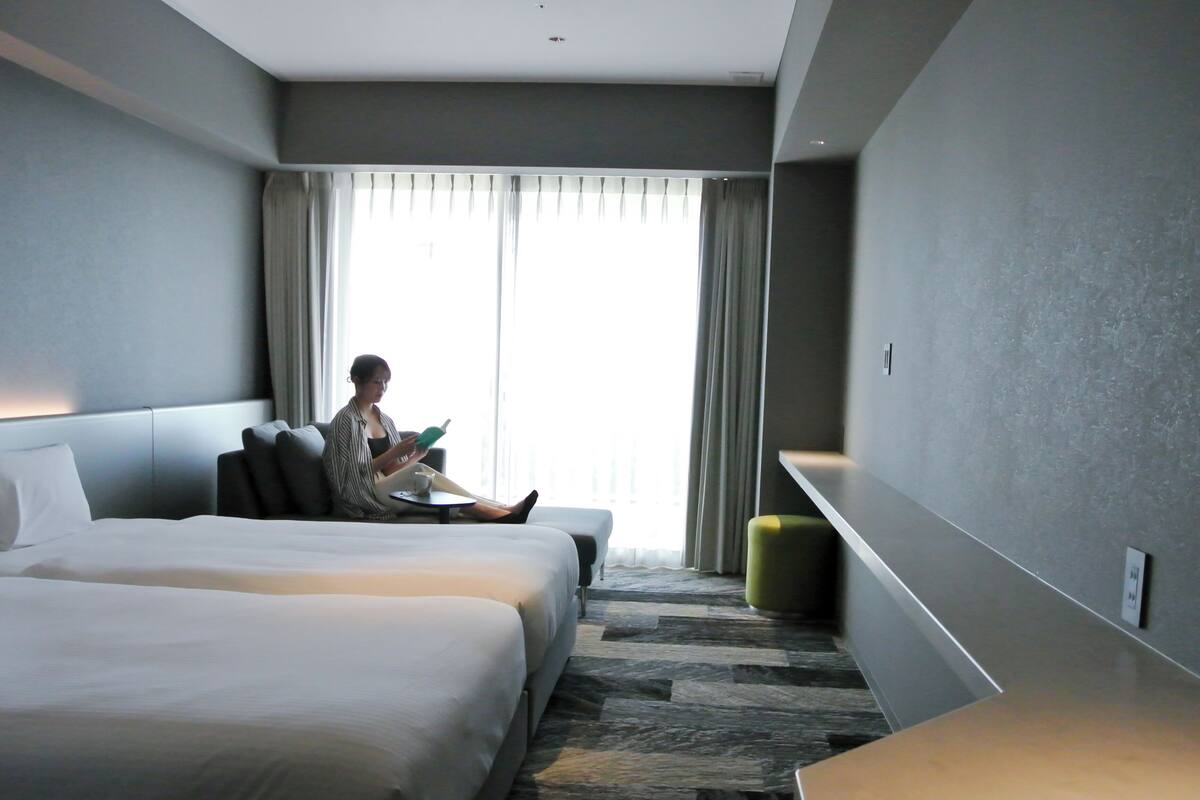 A hotel room with a large bed, a smaller bed, a seating area, and a view of the outdoors.