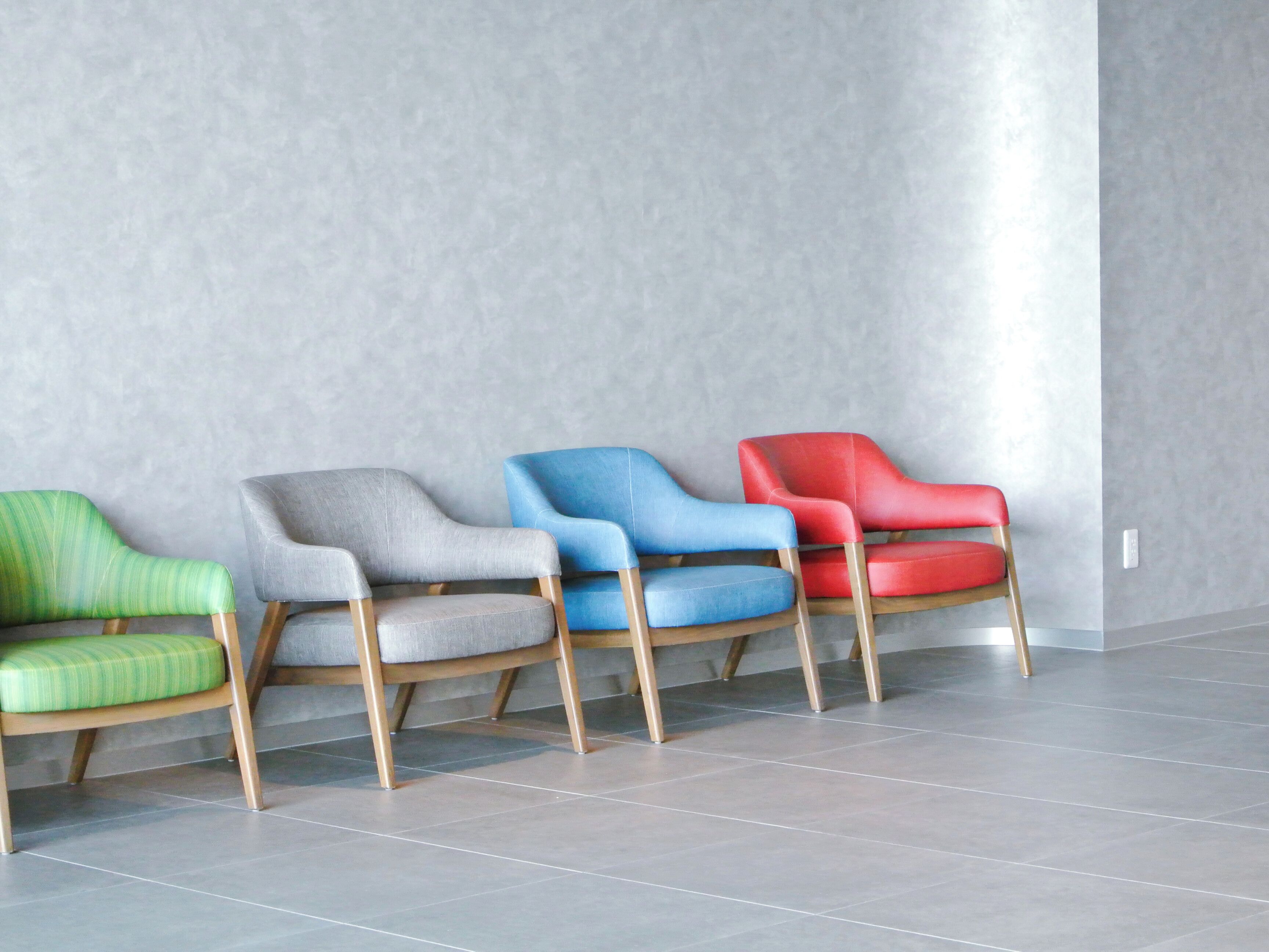 Four chairs in a row with a grey wall and tiled floor.
