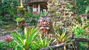 A lush garden with a wooden structure and a large, ornate mask sculpture. - ASBO STAY HOTEL (Kin)