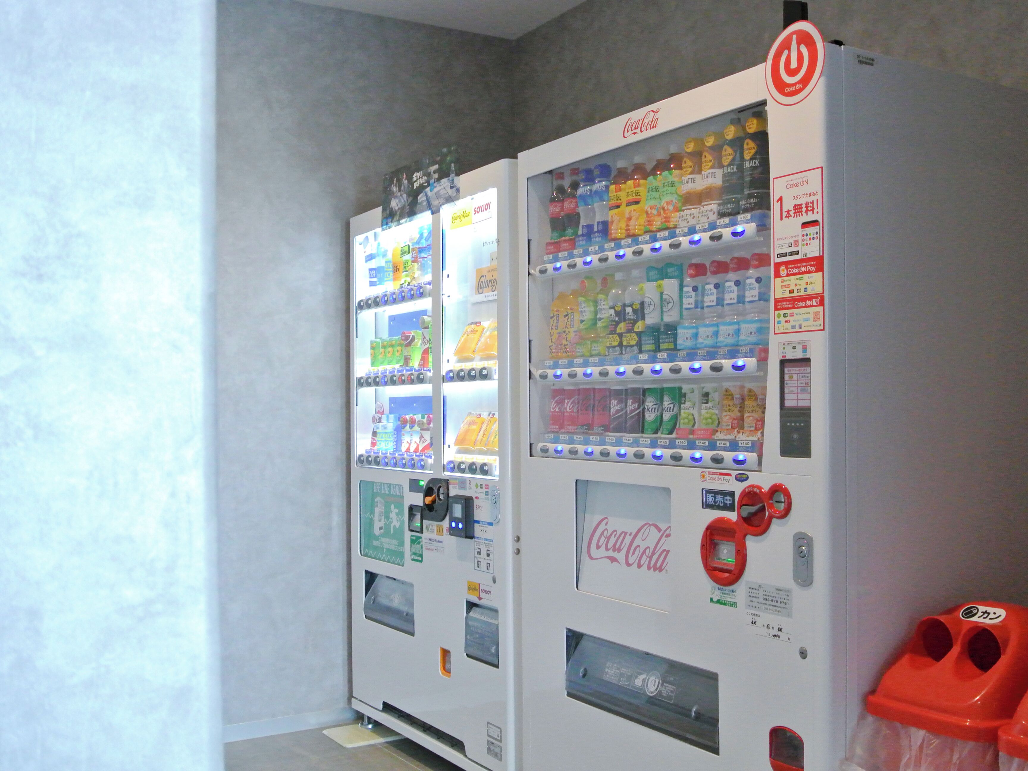 Dos máquinas expendedoras de Coca-Cola con diversas opciones de bebidas y una interfaz de pago.