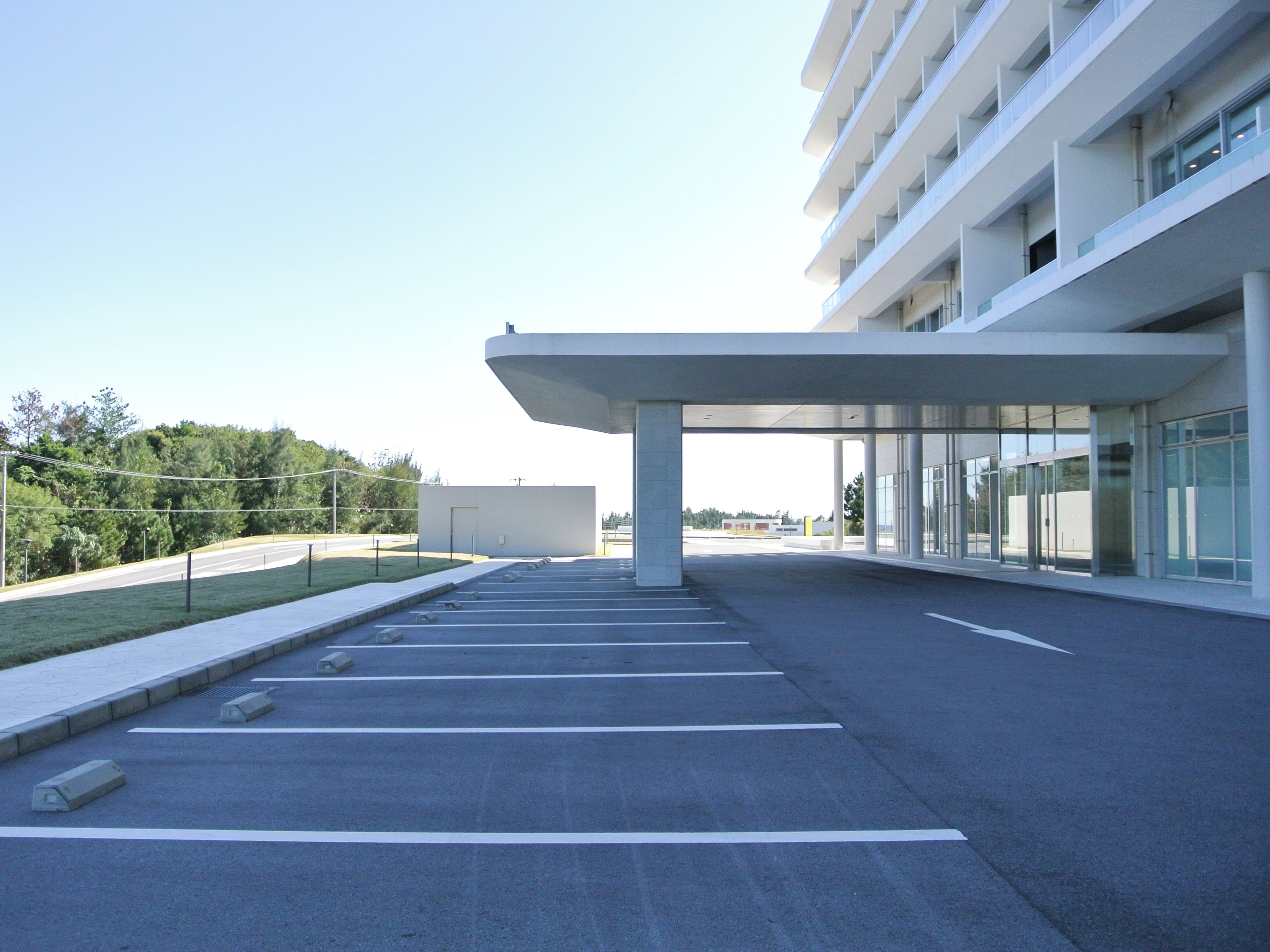 A modern building with a covered entrance, a parking lot, and a clear sky.