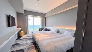 A modern hotel room with a large bed, a flat-screen TV, a bedside table, and a view of the ocean. - ASBO STAY HOTEL (Kin)