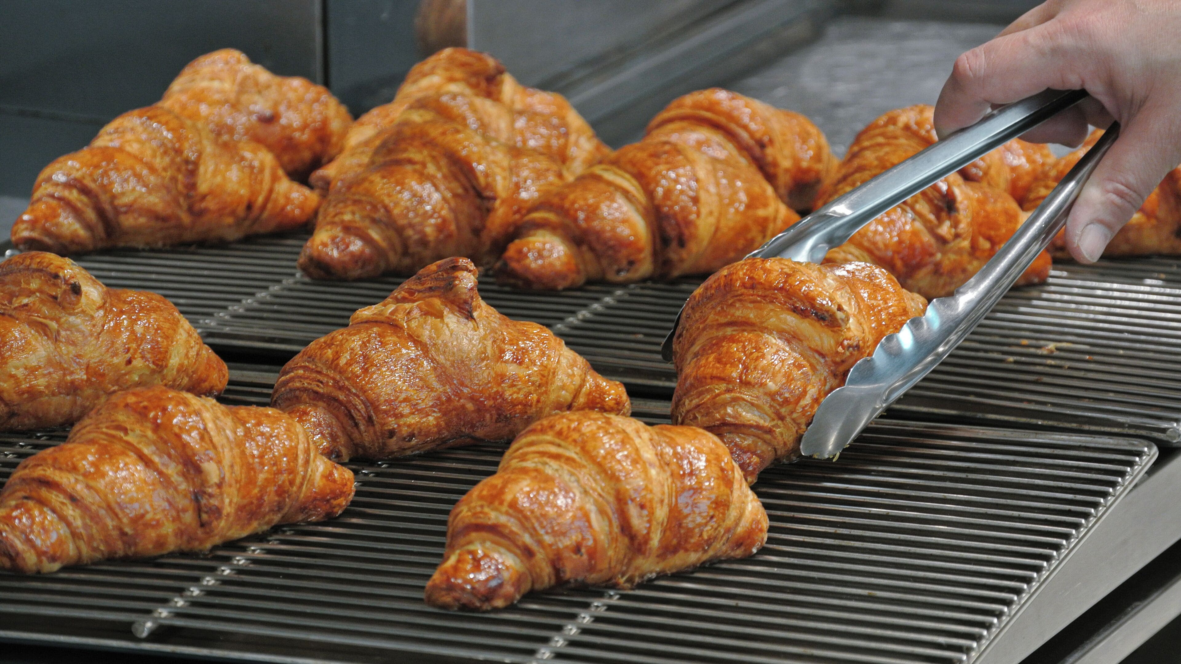 A hand using tongs to handle croissants on a grill.