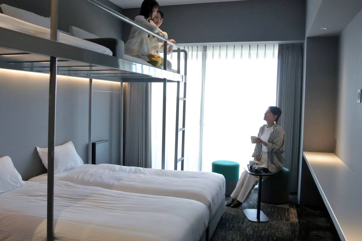 A hotel room with bunk beds, a small round table, and a view of the outdoors.