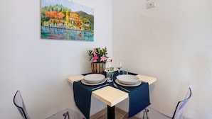 Uma sala de jantar com uma mesa posta para dois, um quadro na parede e um vaso com flores.