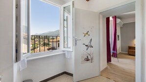Quarto com janela, porta decorada com um mural de pato, lixeira e vista para edifícios e montanhas.