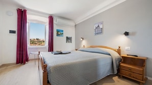 Quarto com cama, mesa de cabeceira, cadeira e janela com cortinas.