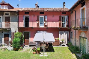 Un edificio di due piani con un balcone, un piccolo giardino e un tavolo con sedie.