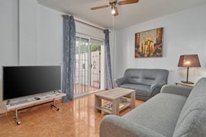 A living room with a flat-screen TV, grey sofa, wooden coffee table, and a ceiling fan. - Holiday Home 'Del Mar Salobreña' with Shared Pool, Private Terrace and Shared Garden (Salobreña)